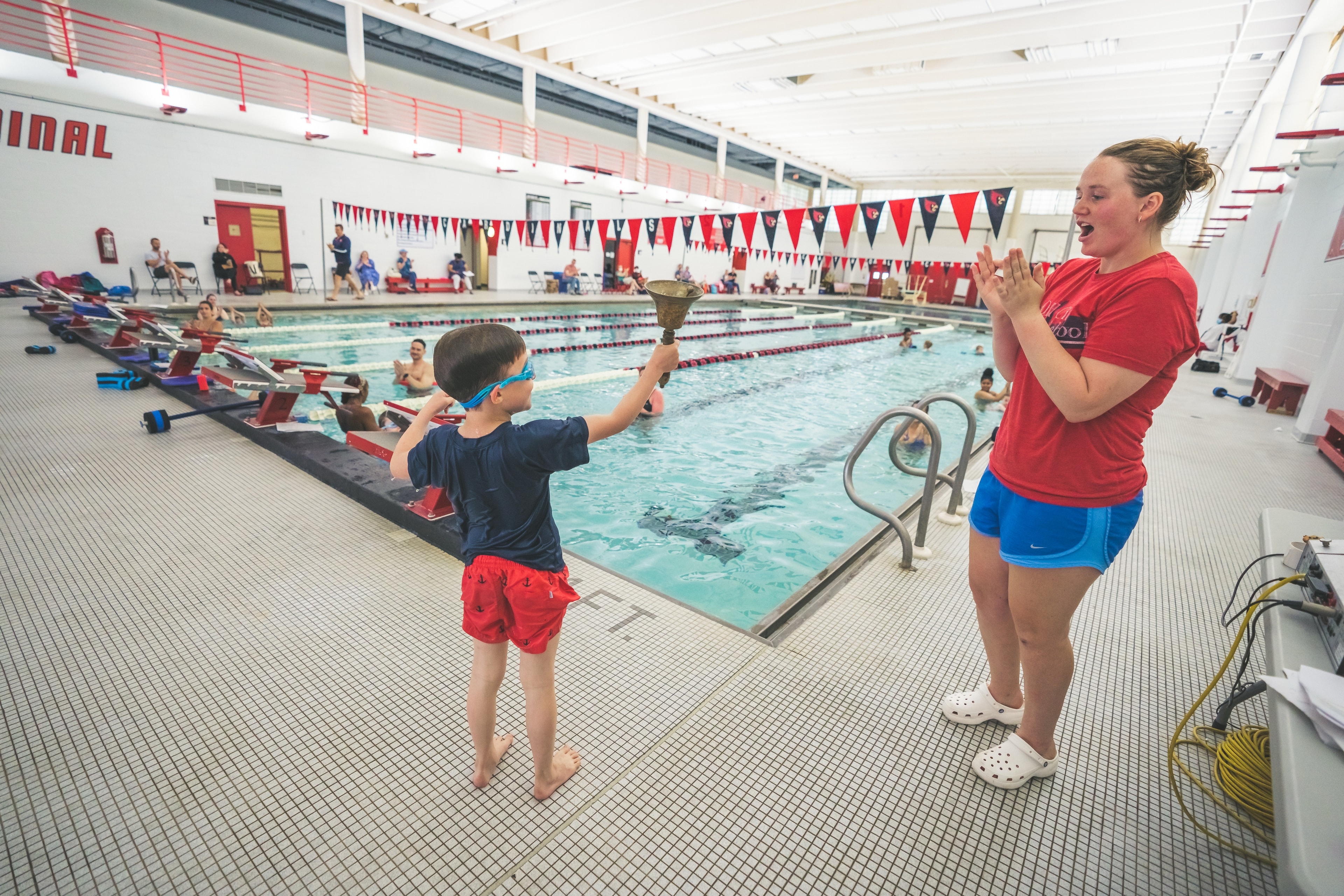 Young swimmer ringing the achievement bell while his coach celebrates at Old City Swim School