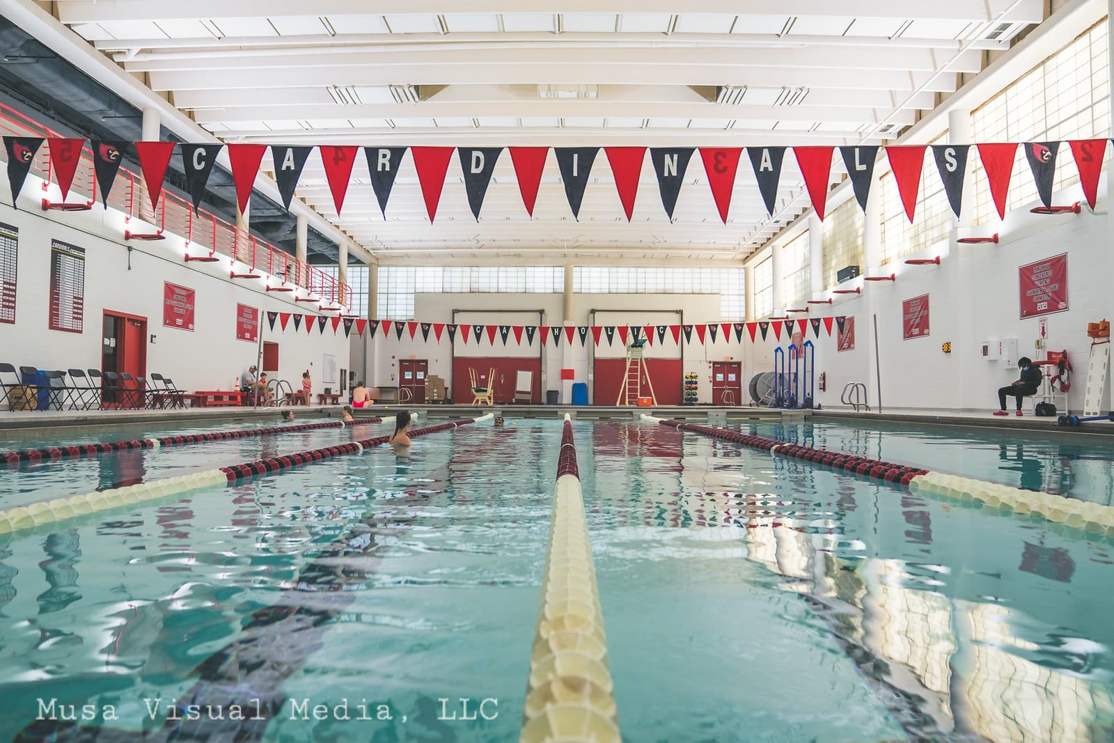 Full pool view from water level at Gallaudet University — pennants spelling CARDINALS overhead, lanes visible, natural light flooding in