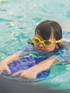 Young swimmer with goggles using a kickboard during stroke development practice