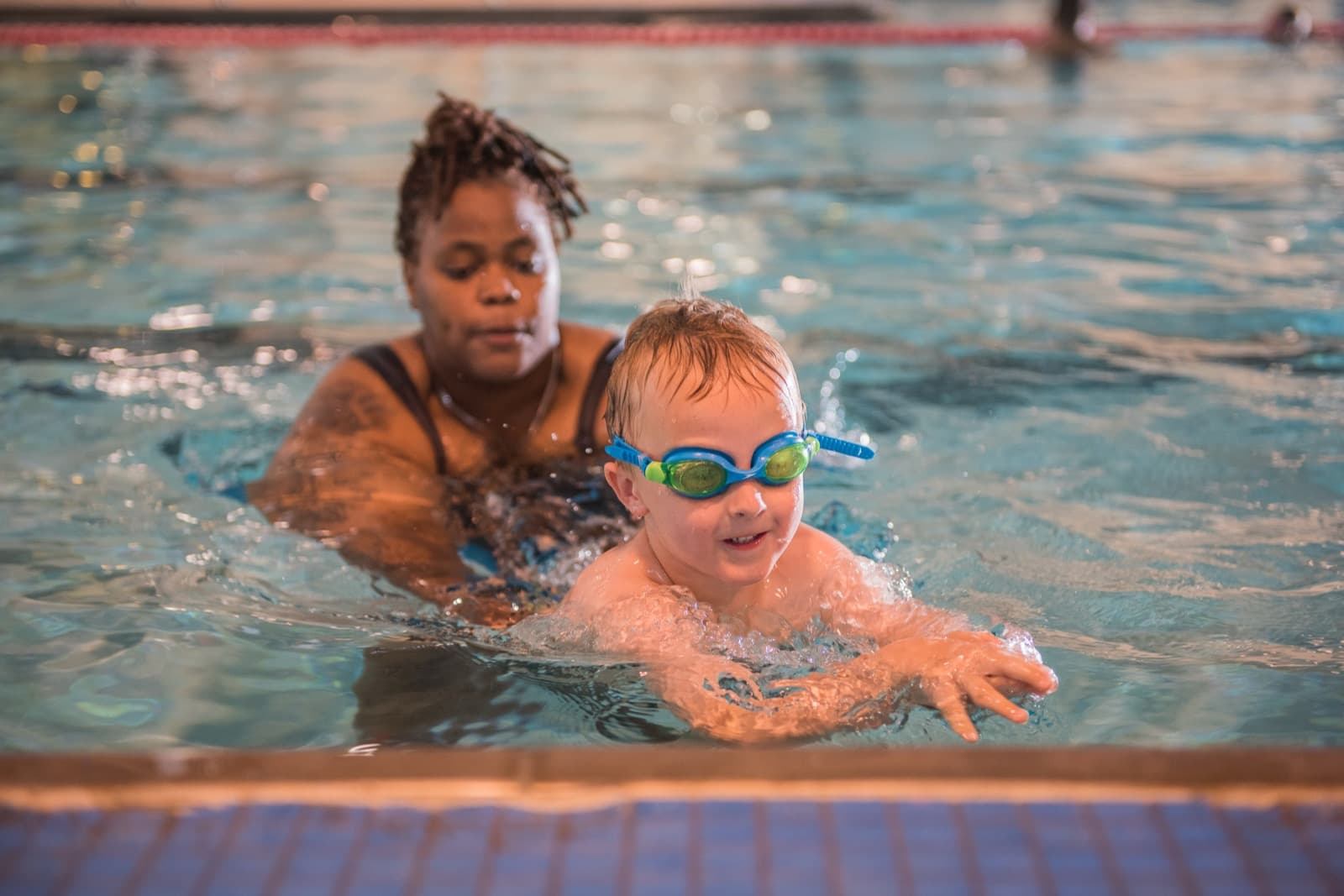 An Old City Swim School coach in the water supporting a young swimmer as he kicks toward the camera