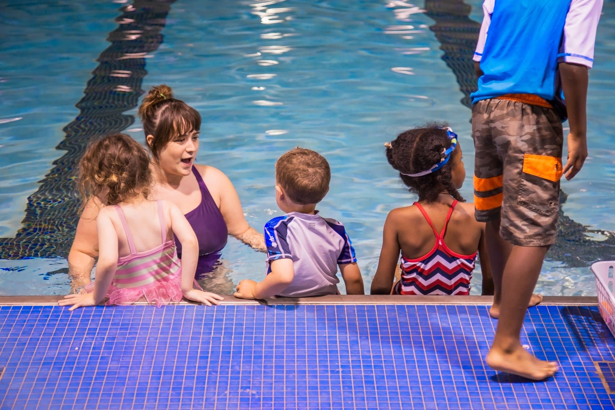 Four small children sitting at the pool edge while an Old City Swim School coach in the water leads the class