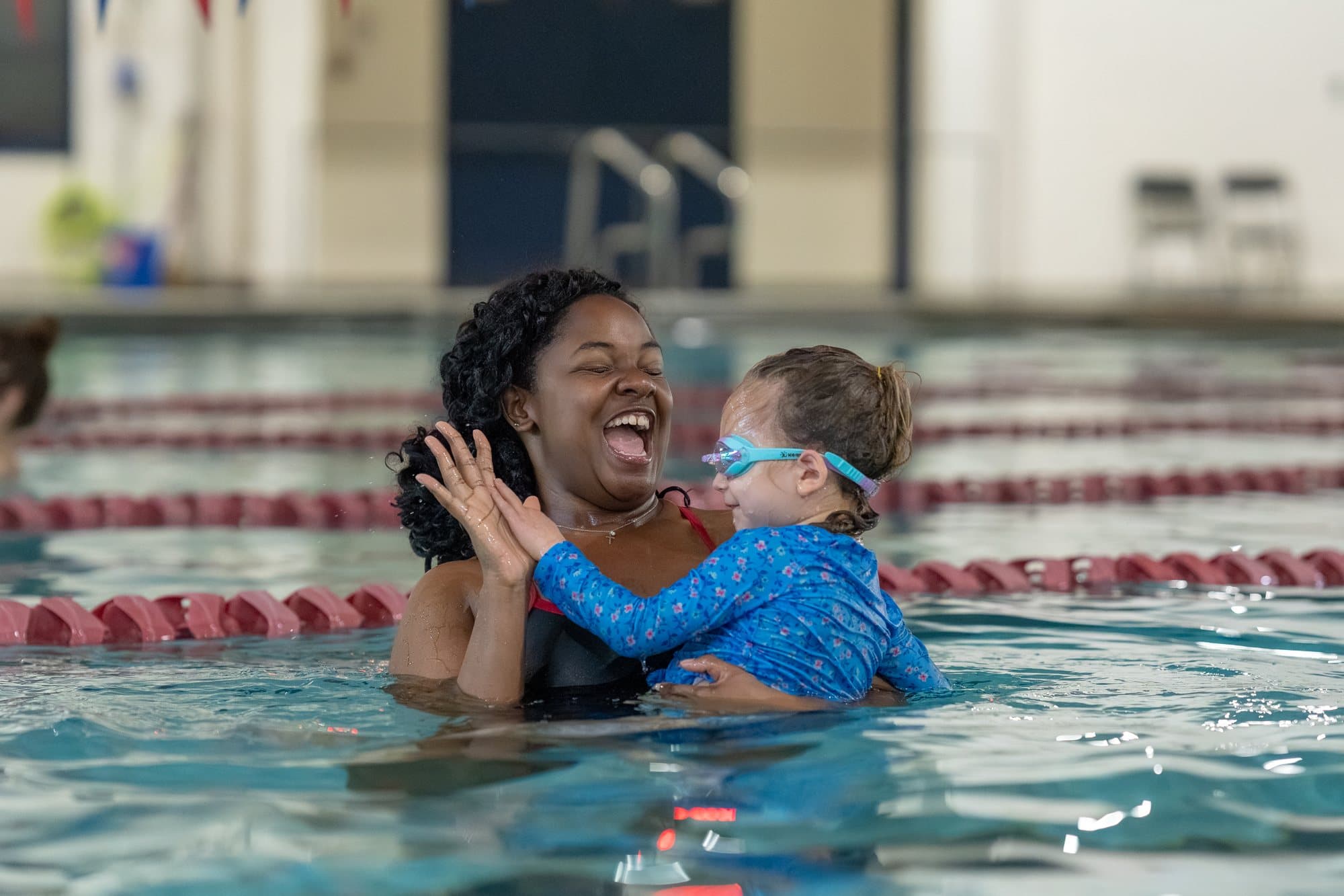 An Old City Swim School coach laughing with a toddler in the pool during a lesson